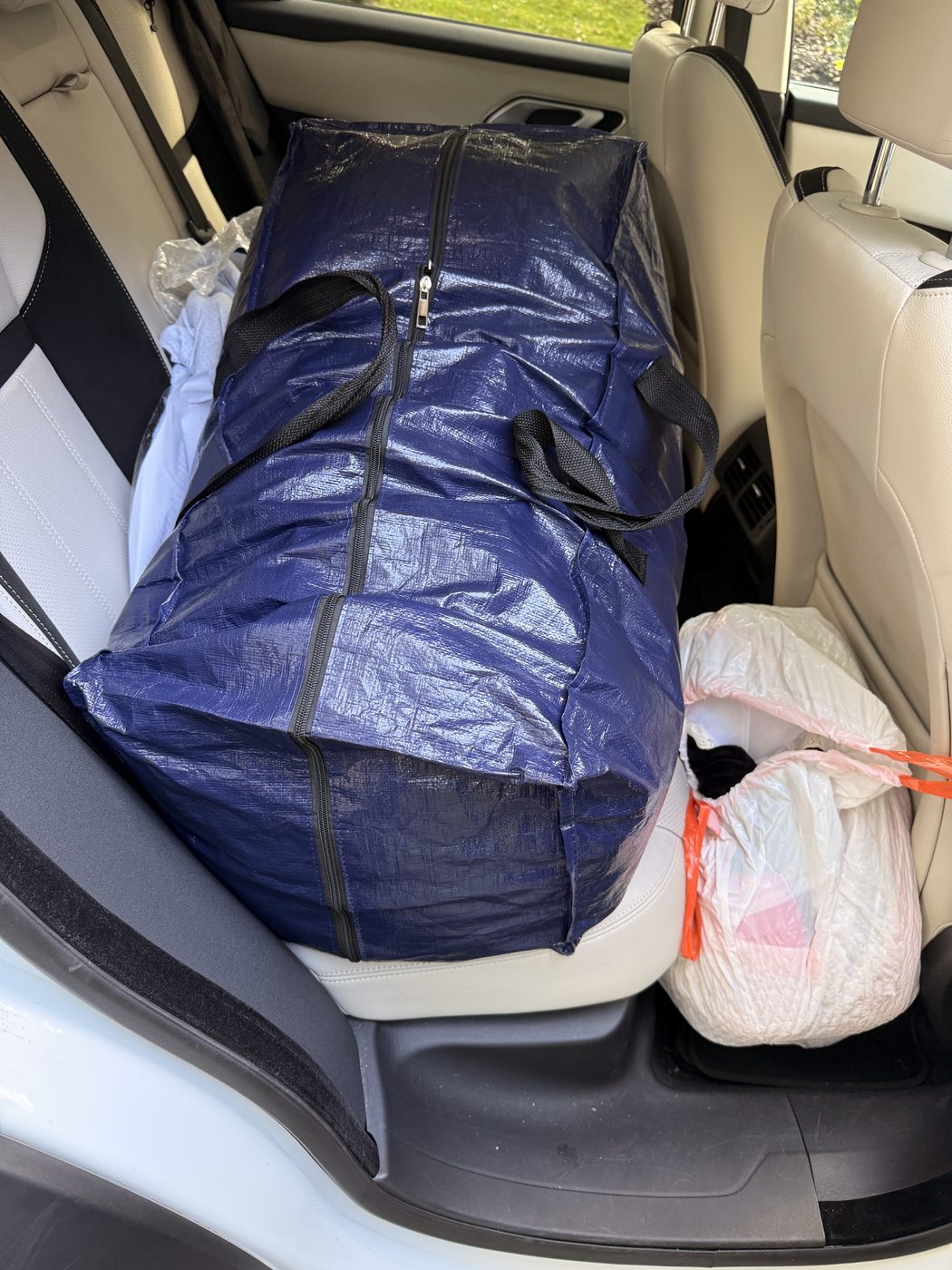 A large blue tote bag and a white bag of donations loaded onto a car seat in Maryland.
